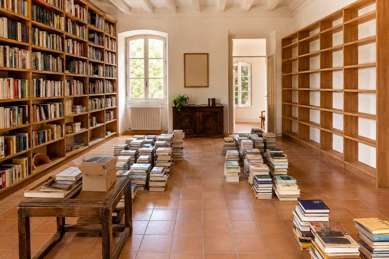 Bibliothèque en cours de vidage, livres empilés au sol devant les rayonnages