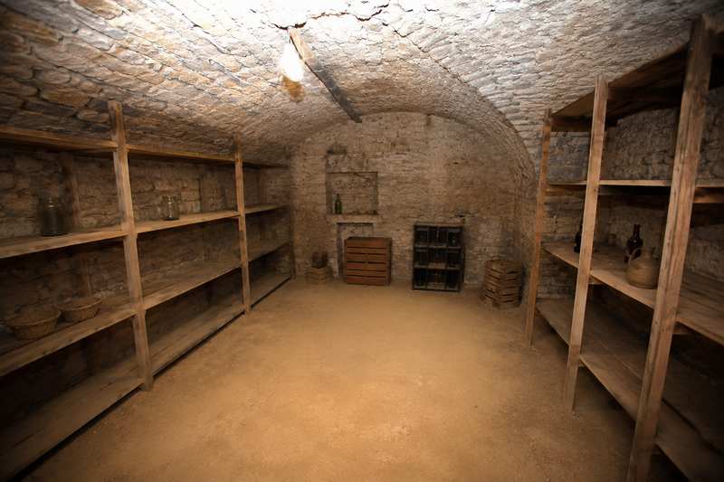 Cave voûtée en pierre éclairée à la baladeuse, étagères de bois chargées