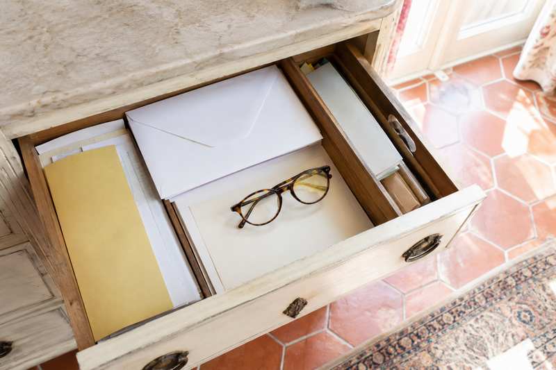 Tiroir de commode ouvert sur des papiers, des enveloppes et une paire de lunettes